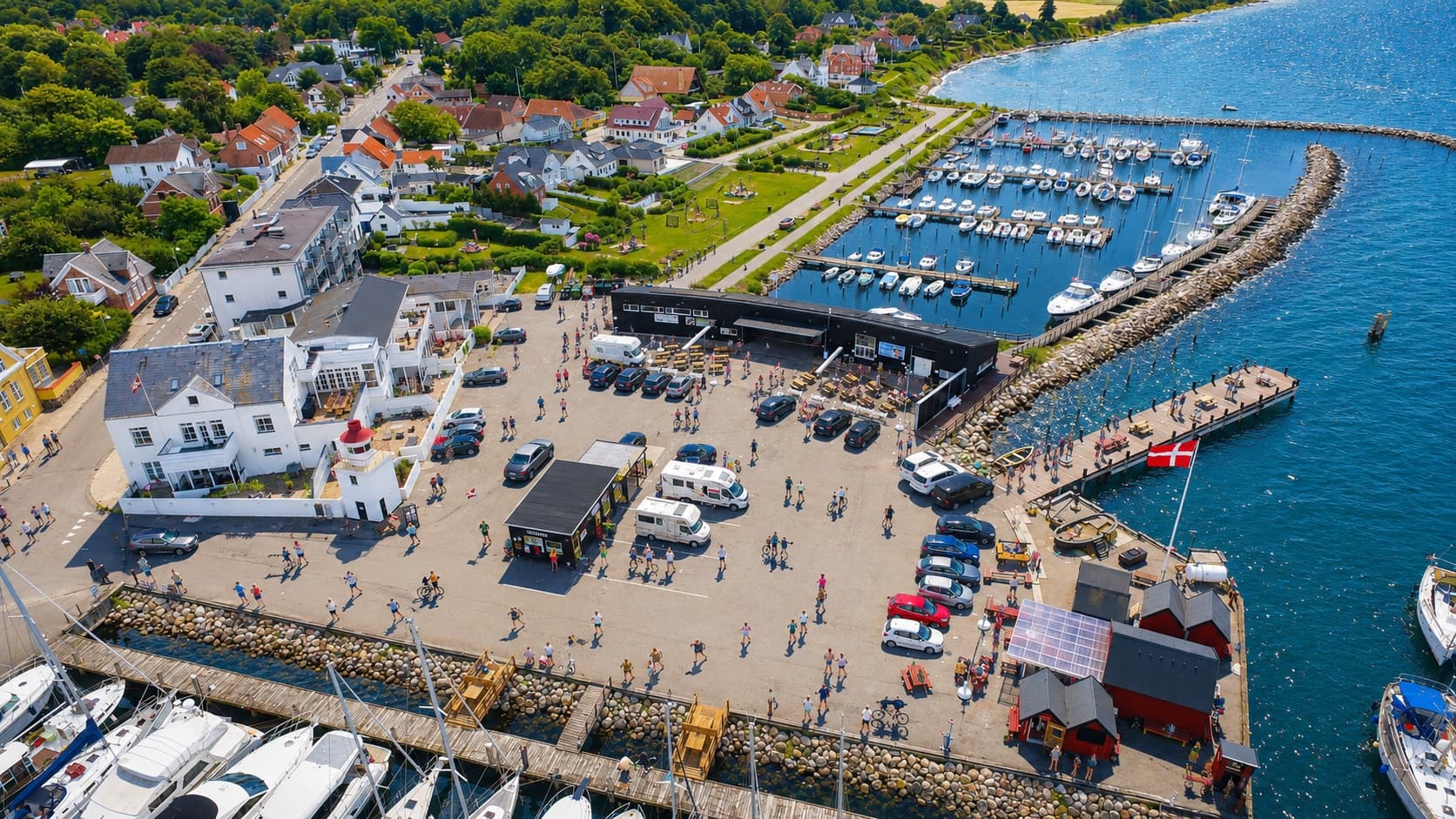 Luftfoto af Lohals Havn en travl sommerdag med lystbåde, torvet fyldt med gæster og solen over vandet