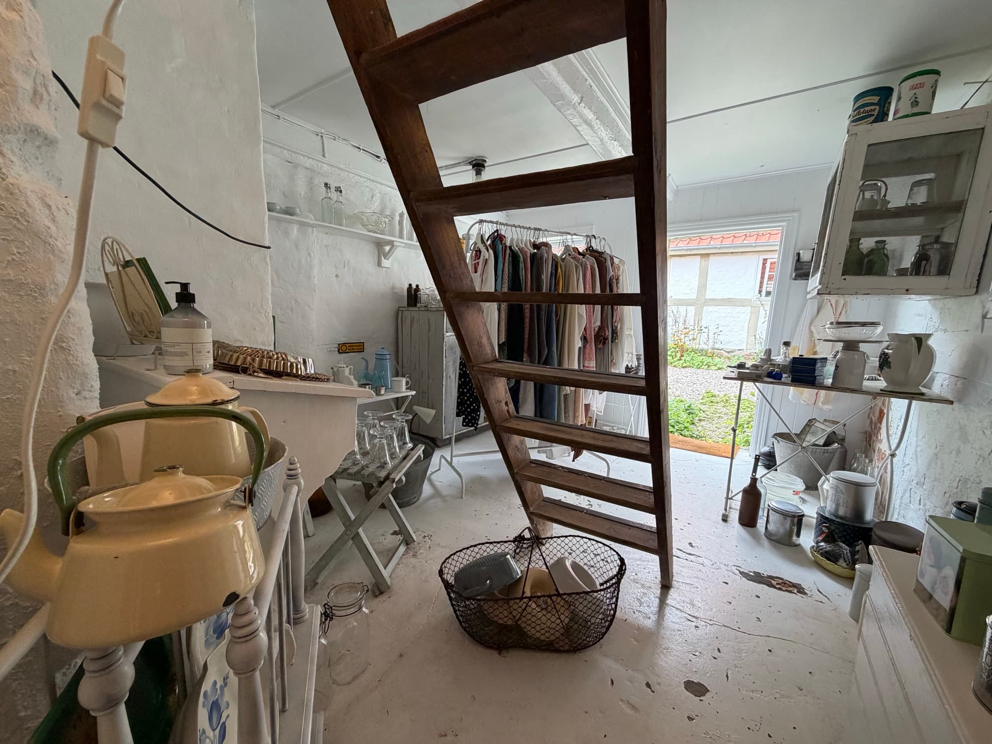 A ladder staircase to the loft with clothing on hangers in the background