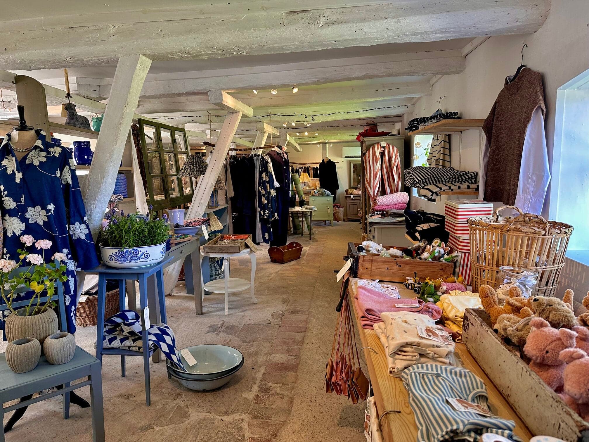 Ladenraum mit geblümten Hemden, blauer Keramik und Kuscheltieren auf den Regalen
