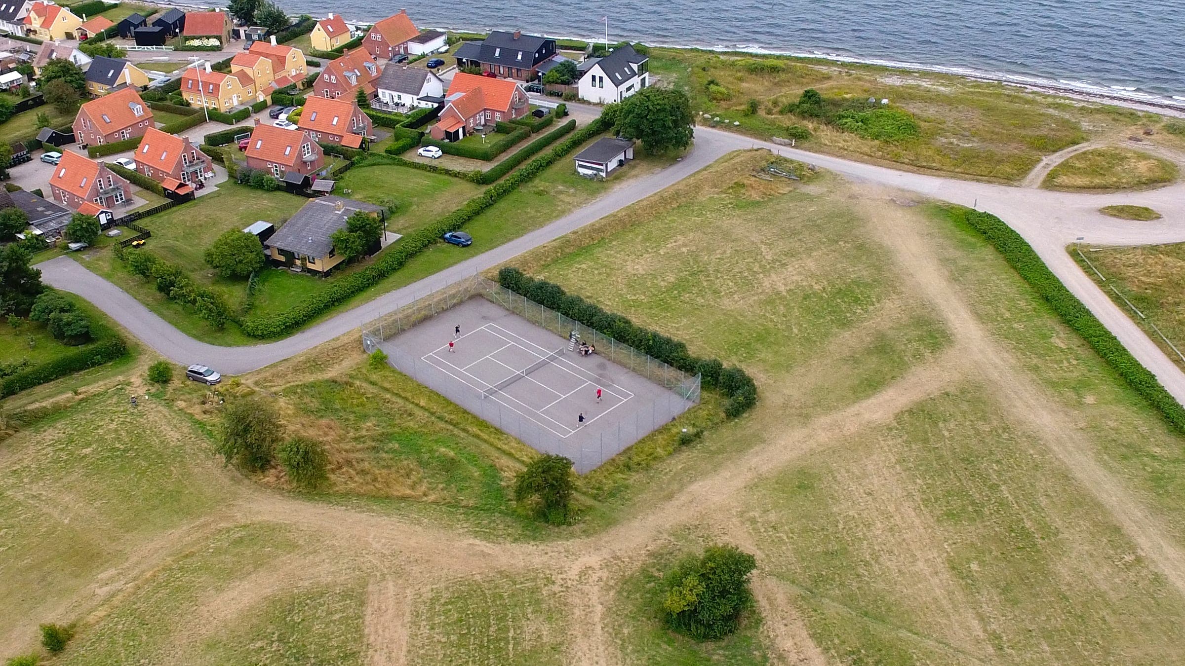 Luftaufnahme des Tennisplatzes bei Lohals Havn, mit dem Ort und der Küste im Hintergrund