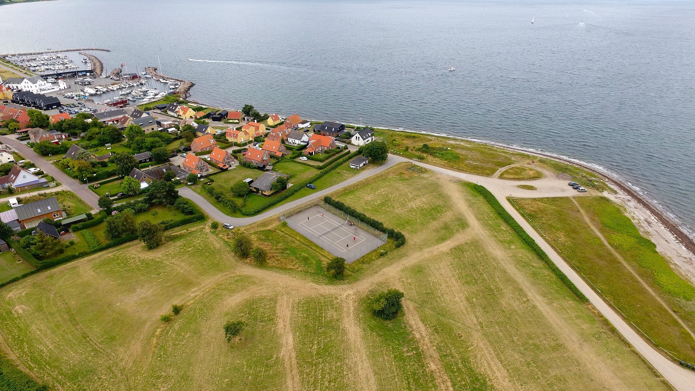 Der Tennisplatz aus der Luft mit dem Hafen und Segelbooten im Hintergrund
